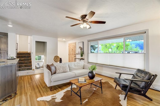 living room with a ceiling fan, stairs, and light wood-style floors