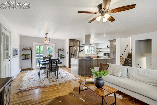 living room featuring french doors, light wood-type flooring, a ceiling fan, stairway, and baseboards
