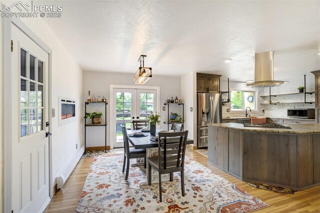 dining room featuring plenty of natural light, light wood-type flooring, french doors, and baseboards