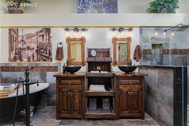 full bath with tile walls, a freestanding tub, a walk in shower, and two vanities
