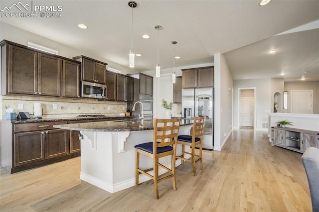 6898 Sedgerock Ln, Colorado Springs, CO 80927 - kitchen featuring appliances with stainless steel finishes, a kitchen bar, dark brown cabinetry, light wood finished floors, and dark stone counters