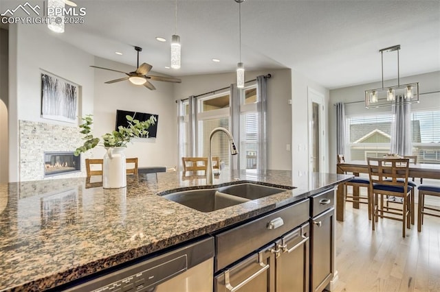6898 Sedgerock Ln, Colorado Springs, CO 80927 - kitchen with a sink, light wood-style flooring, a glass covered fireplace, decorative light fixtures, and dark stone countertops