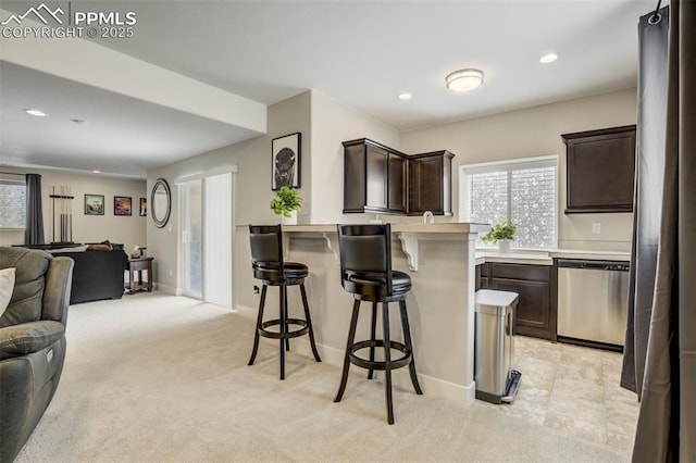 6898 Sedgerock Ln, Colorado Springs, CO 80927 - kitchen featuring stainless steel dishwasher, open floor plan, a kitchen bar, dark brown cabinetry, and light countertops