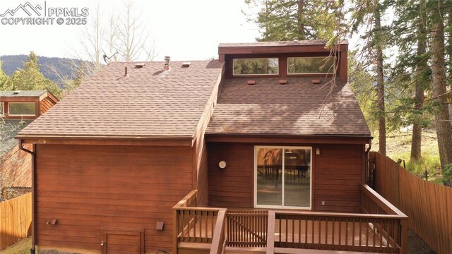 view of front of house featuring roof with shingles, fence, and a wooden deck