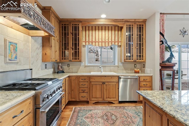 kitchen with stainless steel appliances, a sink, light wood-style floors, glass insert cabinets, and recessed lighting