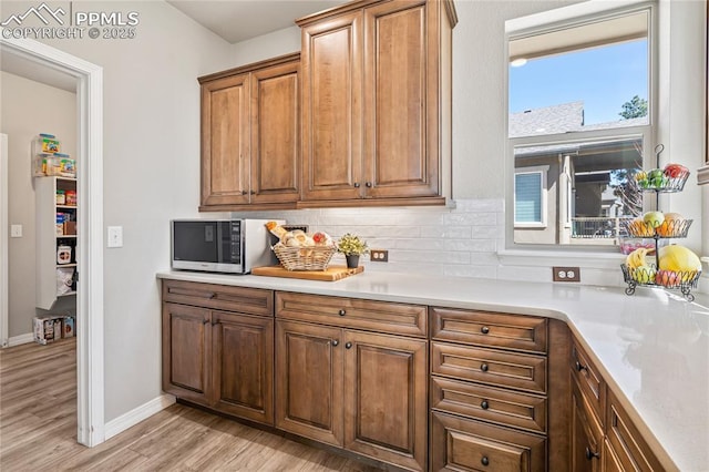 16231 Thunder Cat Way, Monument, CO 80132 - kitchen with stainless steel microwave, light wood-type flooring, decorative backsplash, light countertops, and brown cabinets