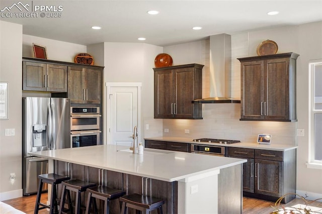 16420 Mountain Glory Dr, Monument, CO 80132 - kitchen with appliances with stainless steel finishes, wall chimney range hood, a sink, a center island with sink, and decorative backsplash