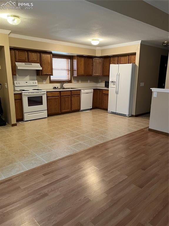 kitchen featuring white appliances, under cabinet range hood, crown molding, a sink, and light countertops
