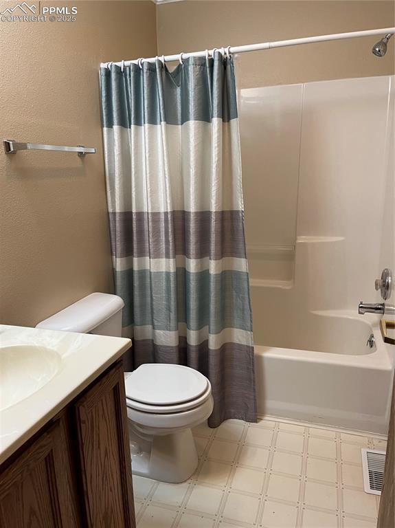 bathroom with tile patterned floors, toilet, vanity, shower / tub combo, and a textured wall
