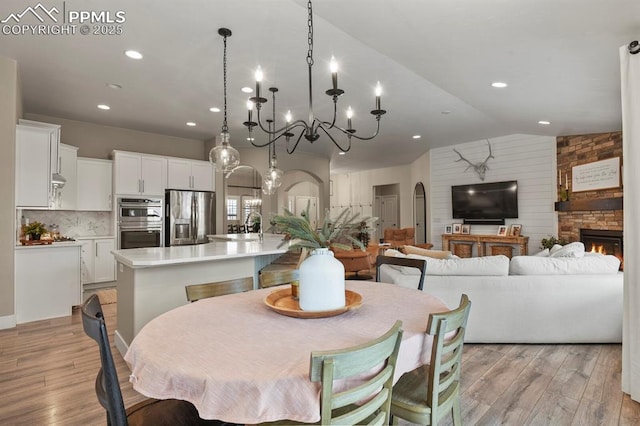 dining room with light wood-type flooring, a chandelier, recessed lighting, lofted ceiling, and arched walkways