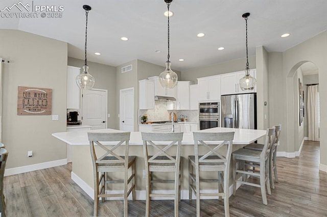 kitchen with stainless steel appliances, arched walkways, light countertops, baseboards, and a large island with sink