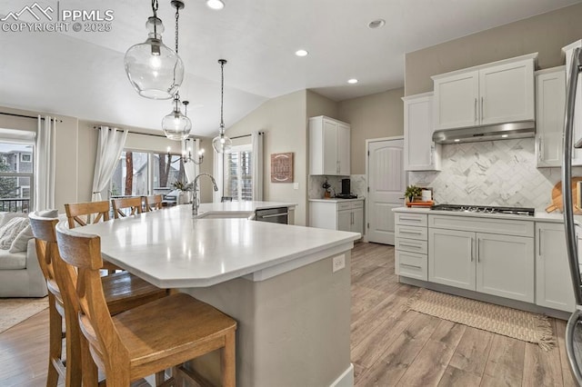 kitchen with under cabinet range hood, a sink, lofted ceiling, stainless steel appliances, and light wood-style floors