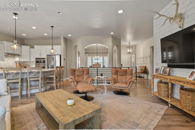 living room with recessed lighting, arched walkways, wood finished floors, and a chandelier