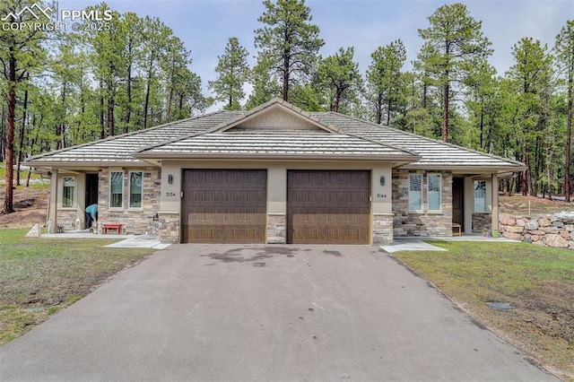 view of front of property featuring stone siding, a garage, driveway, and a tile roof