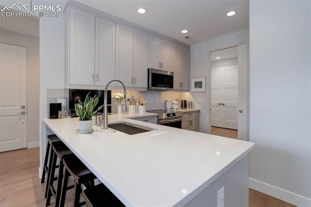 kitchen with stainless steel appliances, a sink, decorative backsplash, light wood finished floors, and baseboards