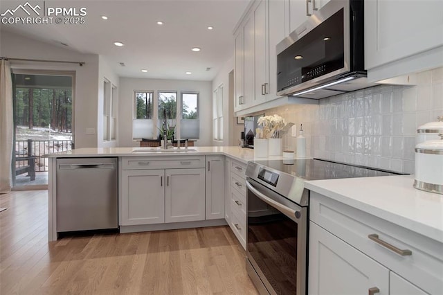 kitchen featuring stainless steel appliances, a peninsula, light wood-style floors, light countertops, and backsplash