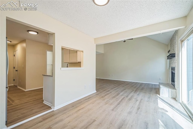 unfurnished living room featuring wood finished floors, a fireplace, a textured ceiling, baseboards, and lofted ceiling