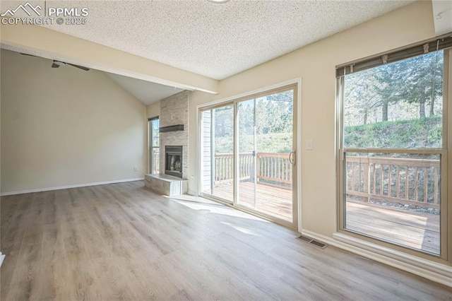 unfurnished living room with wood finished floors, a textured ceiling, baseboards, vaulted ceiling, and a stone fireplace