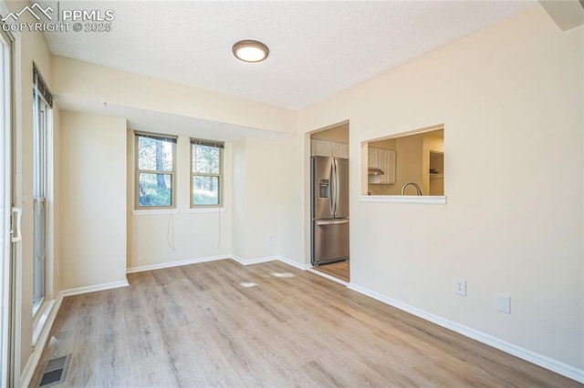 spare room featuring light wood-style floors, a textured ceiling, and baseboards