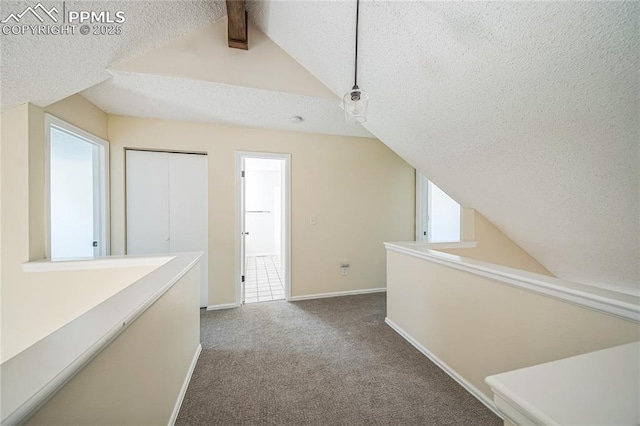 corridor with vaulted ceiling, a textured ceiling, carpet, and baseboards