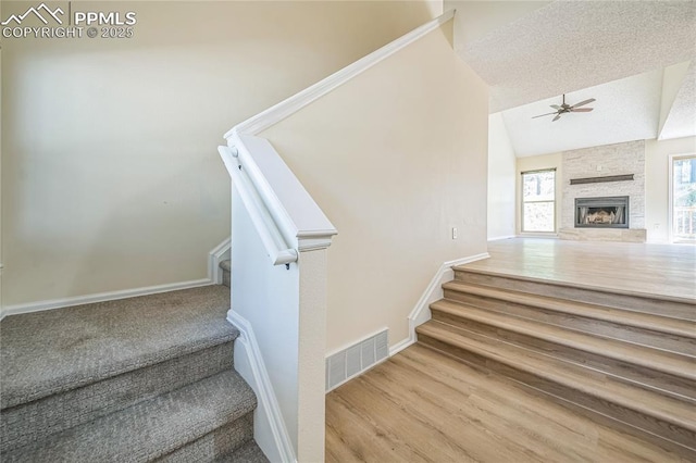 staircase with ceiling fan, baseboards, a stone fireplace, wood finished floors, and lofted ceiling