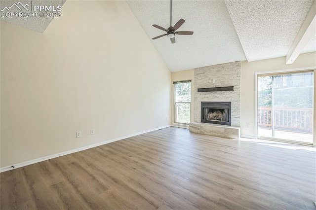 unfurnished living room with a textured ceiling, a ceiling fan, wood finished floors, high vaulted ceiling, and a stone fireplace