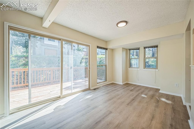 empty room featuring a textured ceiling, wood finished floors, baseboards, and beamed ceiling