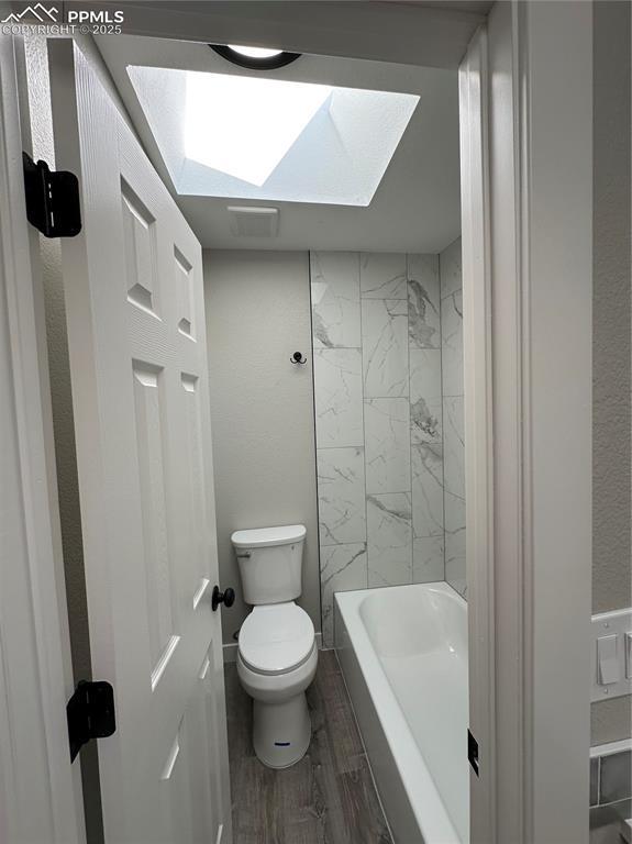 bathroom with toilet, wood finished floors, a skylight, and tub / shower combination