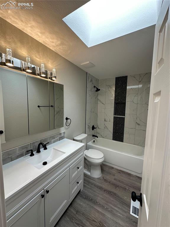 bathroom with wood finished floors, vanity, a skylight, shower / bathtub combination, and toilet