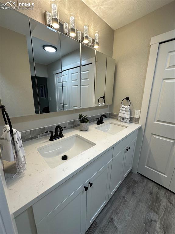 full bathroom with wood finished floors, double vanity, and a textured ceiling