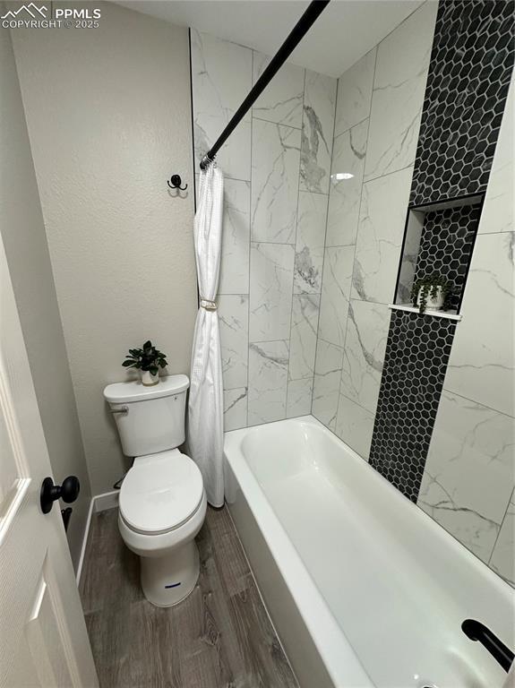 bathroom with shower / bathtub combination with curtain, toilet, wood finished floors, and baseboards
