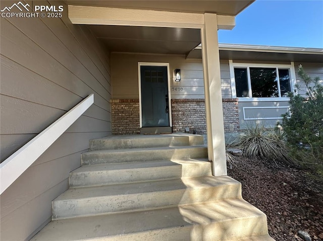 doorway to property featuring a porch and brick siding