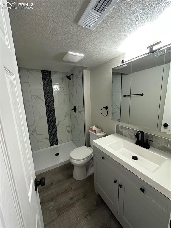 full bathroom with a textured ceiling, a marble finish shower, wood finished floors, vanity, and toilet