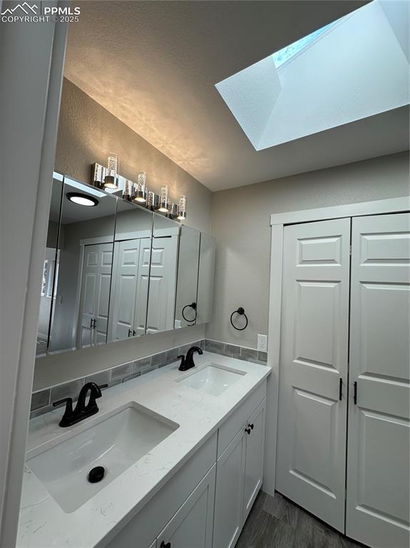 full bath with a skylight, wood finished floors, and double vanity