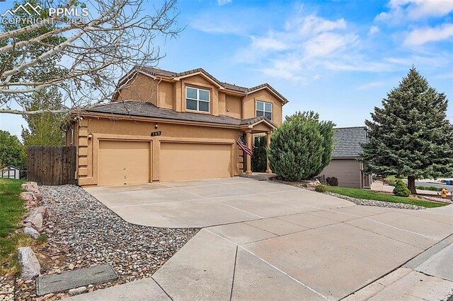 traditional-style house with driveway, stucco siding, fence, a tile roof, and an attached garage