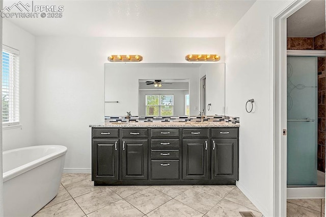 full bath featuring ceiling fan, a stall shower, double vanity, a freestanding bath, and baseboards