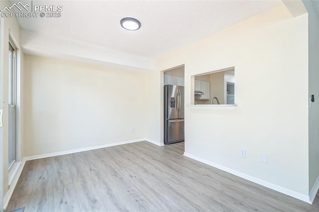 empty room with a textured ceiling, wood finished floors, and baseboards