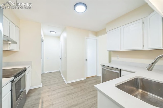 kitchen featuring stainless steel appliances, under cabinet range hood, light wood finished floors, a sink, and white cabinets