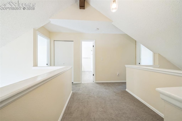 corridor with a textured ceiling, carpet floors, baseboards, and vaulted ceiling