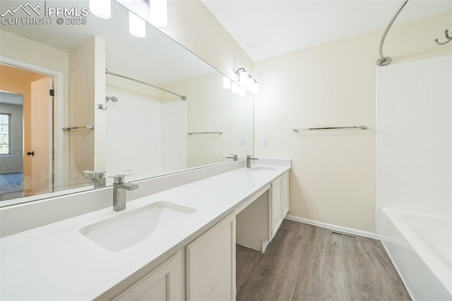 bathroom with wood finished floors, bathing tub / shower combination, double vanity, and baseboards