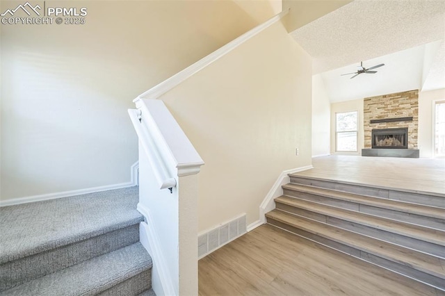stairs featuring a ceiling fan, a stone fireplace, baseboards, vaulted ceiling, and wood finished floors