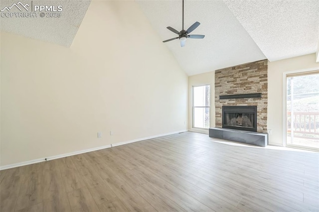 unfurnished living room with a textured ceiling, wood finished floors, a ceiling fan, high vaulted ceiling, and a stone fireplace