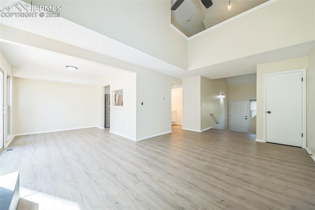 unfurnished living room featuring wood finished floors, ceiling fan, baseboards, and a high ceiling