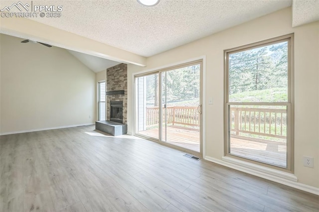 unfurnished living room featuring a textured ceiling, wood finished floors, a fireplace, baseboards, and lofted ceiling