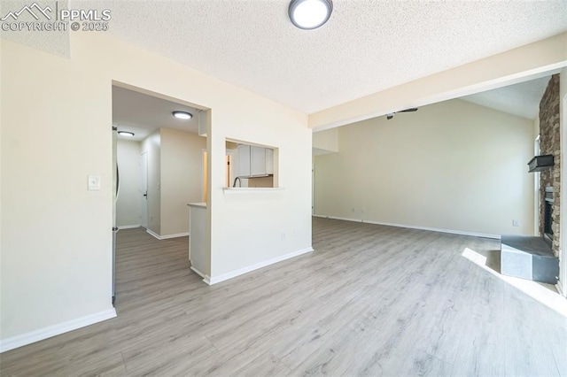 unfurnished living room featuring a large fireplace, wood finished floors, a textured ceiling, and baseboards
