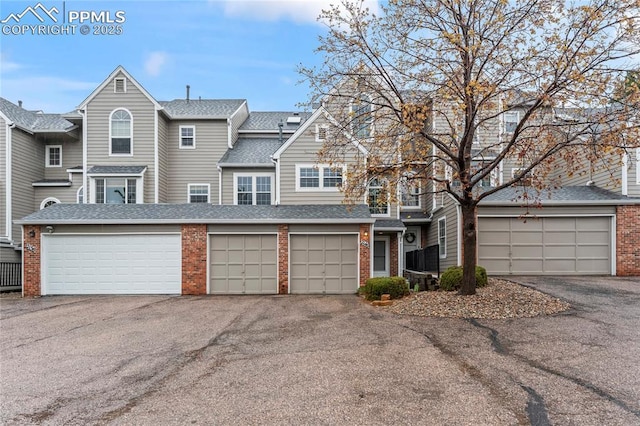 townhome / multi-family property with brick siding, roof with shingles, and driveway