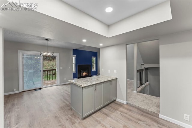 kitchen featuring gray cabinetry, light wood finished floors, baseboards, a lit fireplace, and a chandelier
