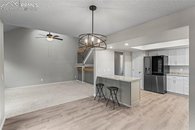 kitchen featuring refrigerator with ice dispenser, light wood-style floors, ceiling fan, a breakfast bar area, and white cabinets