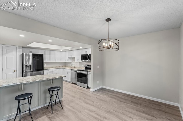 kitchen with stainless steel appliances, a sink, baseboards, light wood-style floors, and a kitchen bar
