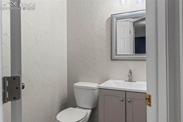 bathroom featuring toilet, vanity, and a textured wall